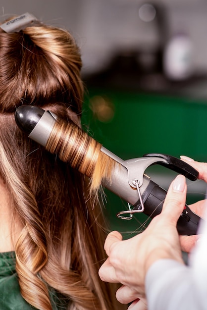 A cabeleireira está enrolando o cabelo para uma jovem caucasiana de cabelos castanhos em um salão de beleza