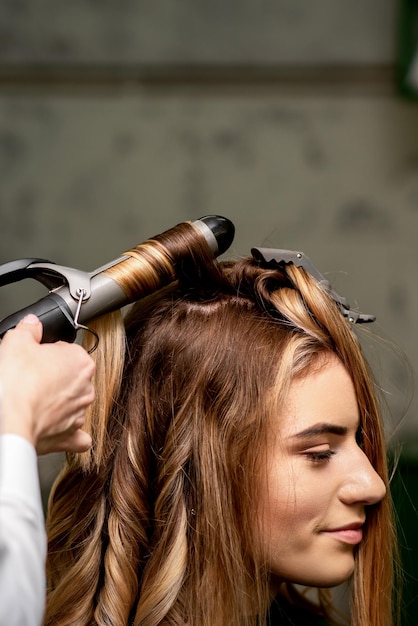 A cabeleireira está enrolando o cabelo para uma jovem caucasiana de cabelos castanhos em um salão de beleza