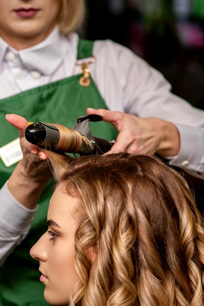 A cabeleireira está enrolando o cabelo para uma jovem caucasiana de cabelos castanhos em um salão de beleza
