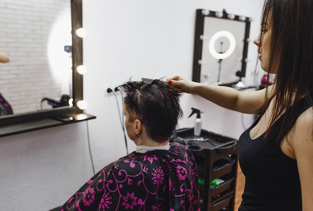 A cabeleireira faz com cuidado um penteado para sua cliente, em um salão de beleza