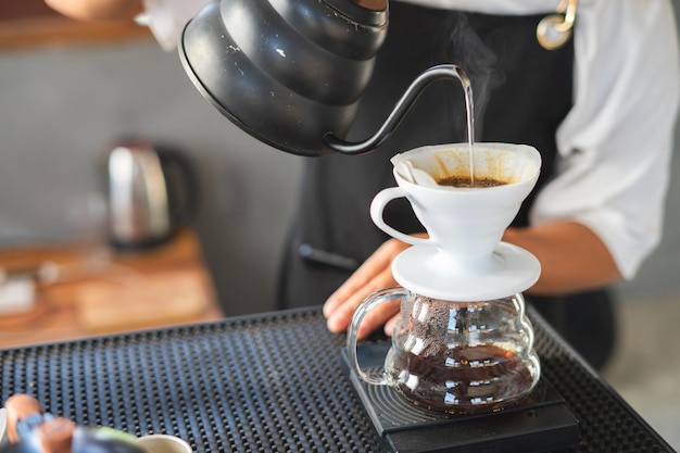 A cafeteira para beber é um café matinal quenteUma mão despejando café fumegante em uma xícara sobre uma mesa de trabalho ao trabalhar em casa