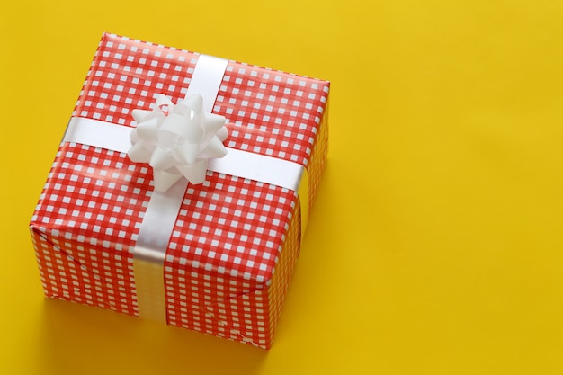 A caixa de presente vermelha do Natal colocada em um assoalho amarelo do papel de arte e tem o espaço da cópia.