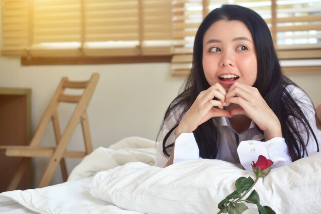 A camisa branca das mulheres da beleza com rosa está no quarto da cama