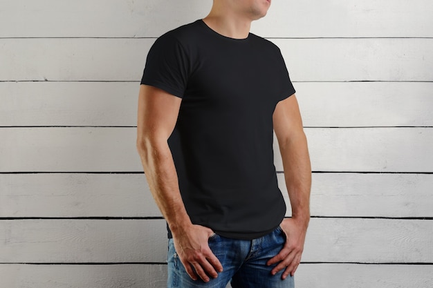 a camiseta preta em um jovem musculoso é meia volta em uma parede de madeira. Roupas de design.