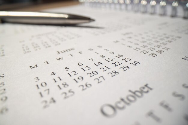 A caneta esferográfica de ferro está na página do bloco de notas com calendário anual sobre a mesa no horário de trabalho do escritório e