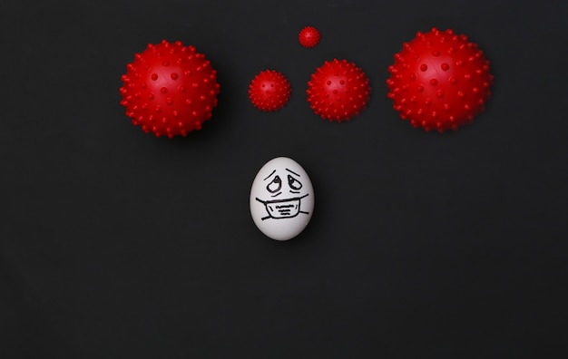 A cara do ovo em uma máscara médica e uma cepa de vírus em fundo preto. pandemia do covid19. vista do topo