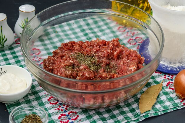 A carne picada está em uma tigela transparente sobre a mesa e preparada para almôndegas e sua assadeira no forno, orientação horizontal