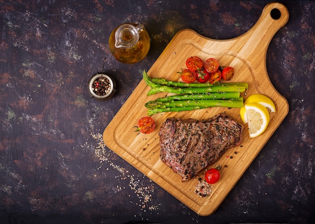 A carne rara do bife suculento com especiarias em uma placa de madeira e decora do aspargo.