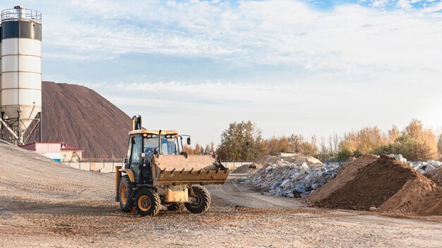 A carregadeira de escavadeira trabalha com um balde para transportar areia em um canteiro de obras. Equipamento de construção profissional para terraplanagem.