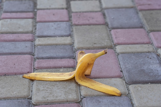 A casca da banana foi deixada na calçada. O perigo pode escorregar. Se alguém pisar nele. Tenha cuidado com o escorregadio. Close up, ao ar livre