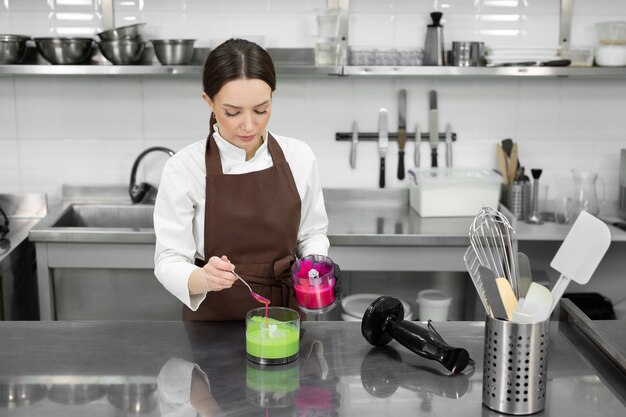 A chef confeiteira pinta um esmalte de espelho em verde e rosa em uma cozinha profissional.