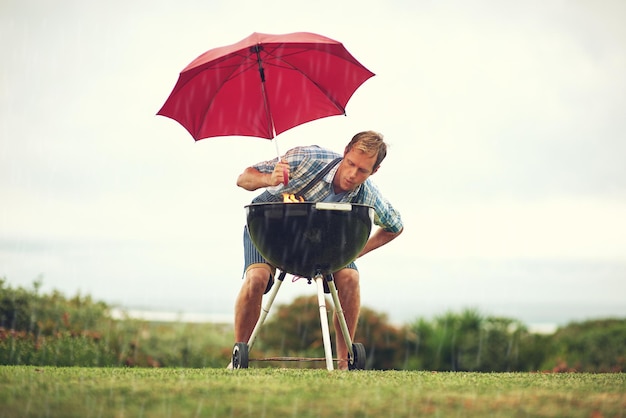 A chuva não vai parar meu churrasco Foto de um homem tentando fazer churrasco na chuva