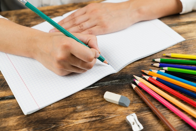 A colegial se senta em sua mesa e desenha em um caderno com lápis de cor.