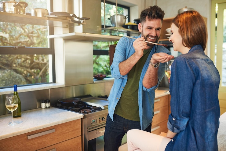 Foto a comida tem um sabor melhor quando é feita com amor foto de um homem dando a sua esposa um gostinho da comida que ele está preparando em casa