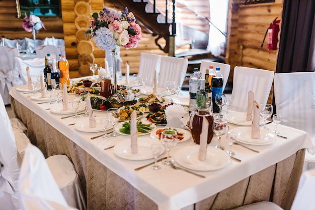 A composição de flores e verde está em uma mesa festiva no salão de banquetes Servindo os convidados à mesa Pratos talheres talheres guardanapo de vidro Decoração da mesa de casamento