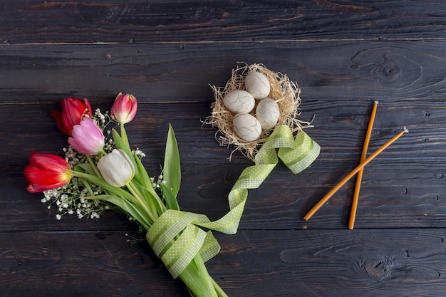 A composição de páscoa Ovos um buquê de tulipas e velas de igreja na mesa de madeira closeup