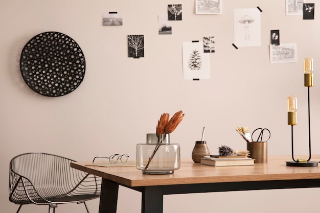 A composição elegante do interior do escritório aconchegante com cartaz de plantas de mesa de madeira de cadeira de metal e acessórios pessoais decoração para casa modelo