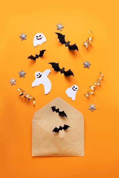 A composição plana leiga de halloween de envelope de papel jangada e morcegos de papel preto voam sobre um fundo laranja, vista superior.