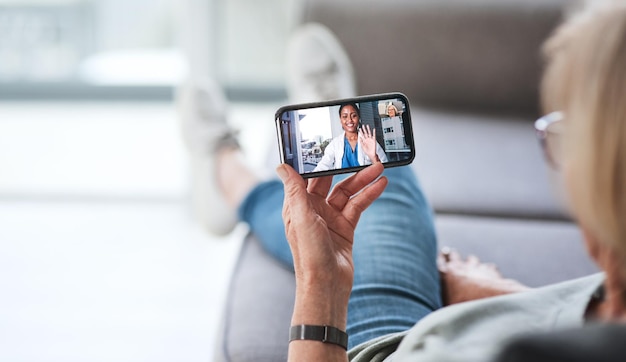 A consulta mais confortável de todos os tempos foto de uma mulher idosa usando um smartphone para fazer uma videochamada com seu médico no sofá de uma casa