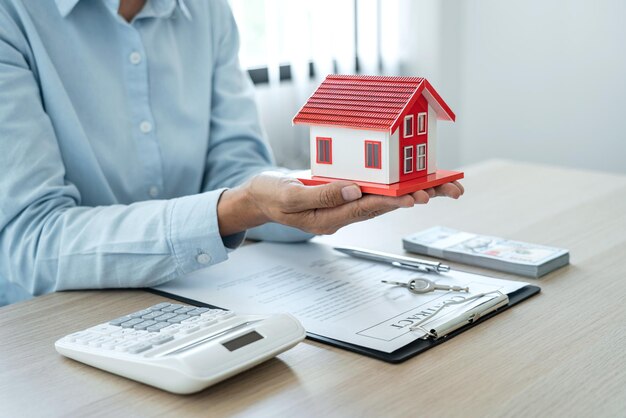 A corretora imobiliária feminina está usando as mãos segurando uma casa de telhado vermelho para o conceito de investimento imobiliário sobre comércio de casas, contrato de compra e seguro de casa