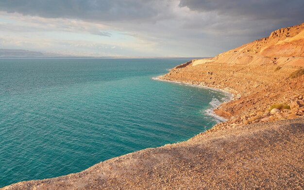 Foto a costa do mar morto do lado da jordânia areia seca e rochas praia sol brilha sobre a bela superfície de água azul