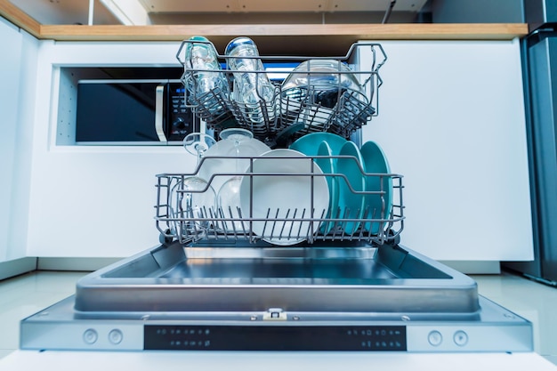 A cozinha branca e a máquina de lavar louça aberta com pratos limpos