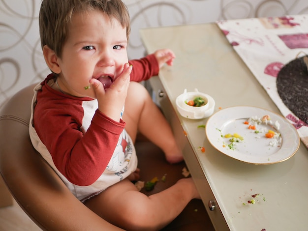 A criança à mesa come legumes. conceito de infância, comida e pessoas - criança tomando café da manhã saudável para o jantar