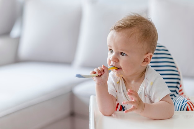 A criança alegre do bebê come o alimento próprio com colher.