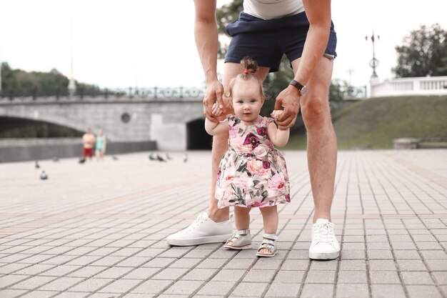 A criança aprende a andar. O pai apóia o filho e o ensina a andar.
