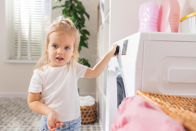 A criança aprende a operar a máquina de lavar uma loira de olhos azuis doce menina de poucos anos