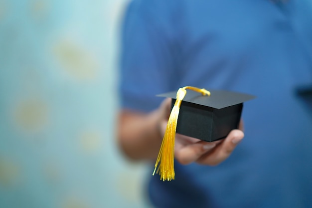 A criança asiática das crianças prende o chapéu da abertura da graduação à disposicão.