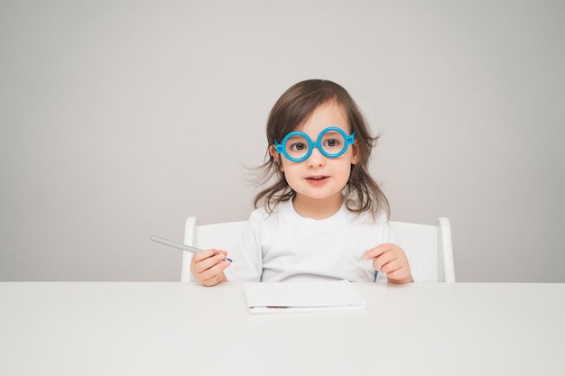 Foto a criança brinca de médico uma menina de óculos de brinquedo azul se senta em uma mesa branca para texto e publicidade.