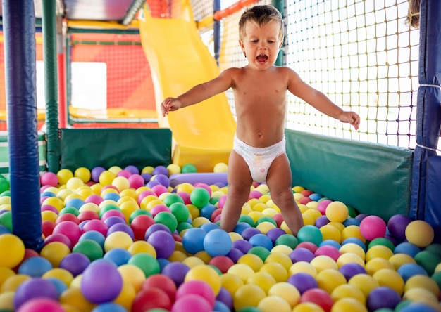 A criança brinca na sala de jogos e desce o escorregador para a piscina com pequenas bolas