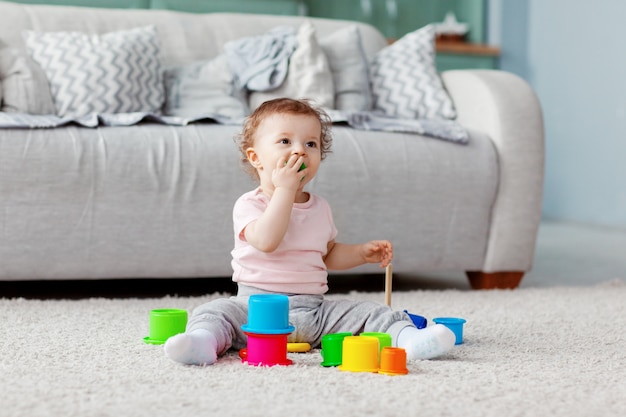 A criança brinca no chão em um tapete leve com brinquedos brilhantes, constrói uma torre