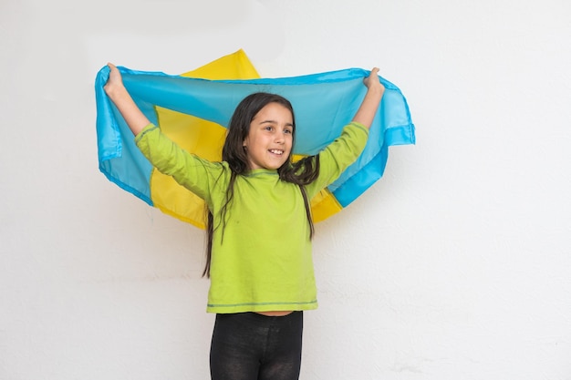 A criança carrega a bandeira azul e amarela esvoaçante da Ucrânia isolada no branco. Dia da Independência da Ucrânia. Dia da Bandeira. Dia da Constituição. Menina no bordado tradicional com bandeira da Ucrânia