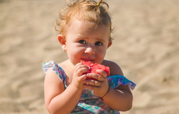 A criança come fruta à beira-mar. Foco seletivo. Criança.