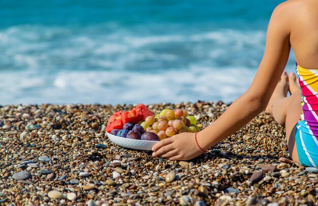 A criança come fruta à beira-mar. Foco seletivo.