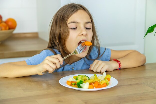 A criança come legumes em uma cadeira Foco seletivo Kid