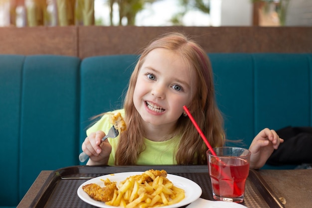 a criança come suco de frango e batatas fritas no refeitório da escola ou café de fast food