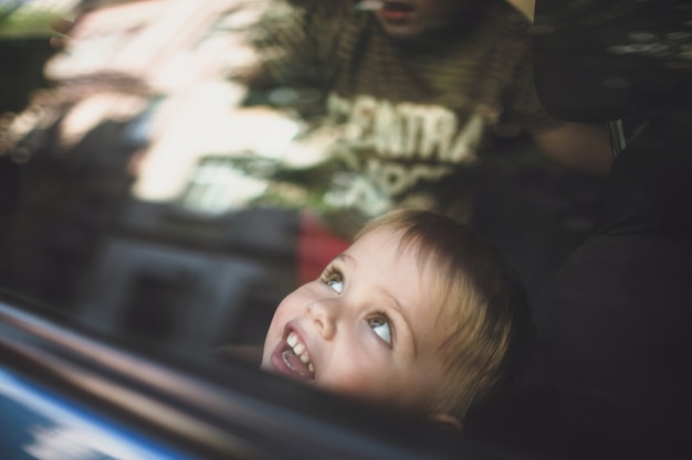 Foto a criança de sorriso olha fora de uma janela do carro