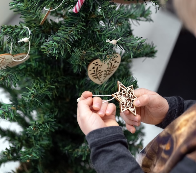 A criança decora a árvore de Natal. As mãos seguram um floco de neve decorativo, uma estrela.