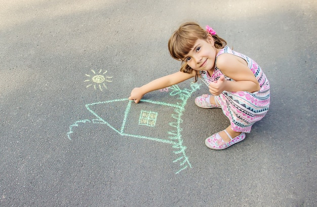A criança desenha a casa com giz no asfalto. Foco seletivo.
