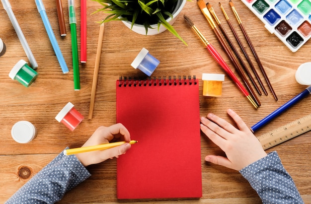 A criança desenha com canetas e tintas de feltro. Mãos de criança com lápis e bloco de notas.