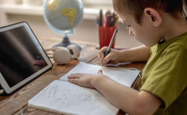 A criança é um menino em uma camiseta verde com fones de ouvido fazendo lição de casa em um tablet conceito de educação escolar remota