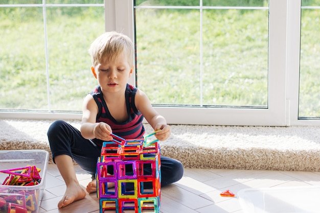 A criança está brincando com um construtor magnético multicolorido, construindo uma torre. Brinquedos educativos. Um bloco de construção para um bebê ou criança pequena Desordem na sala de jogos