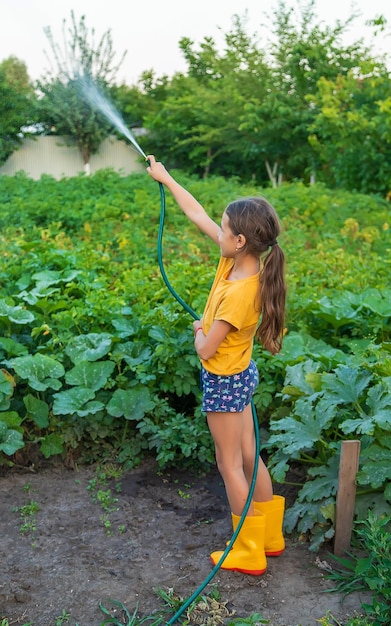 A criança está molhando o jardim com uma mangueira Foco seletivo