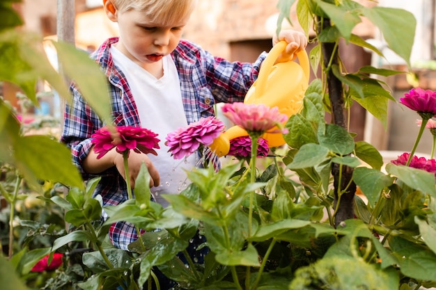 A criança está regando flores no jardim usando uma jarra