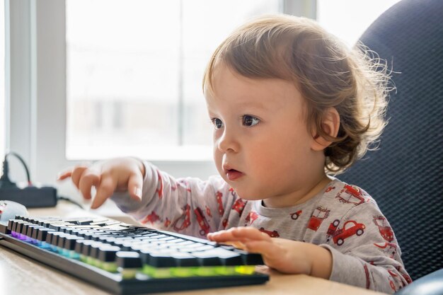 A criança está sentada à mesa com o teclado do computador aprendendo a dominar o computador fechado