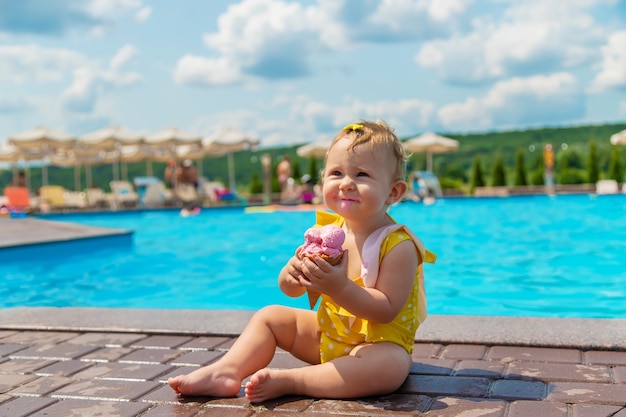 A criança está tomando sorvete perto da piscina. Foco seletivo. Miúdo.