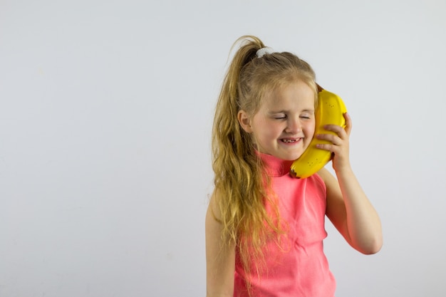 A criança fala em um telefone banana. Menina rindo e brincando. Humor de brincadeira